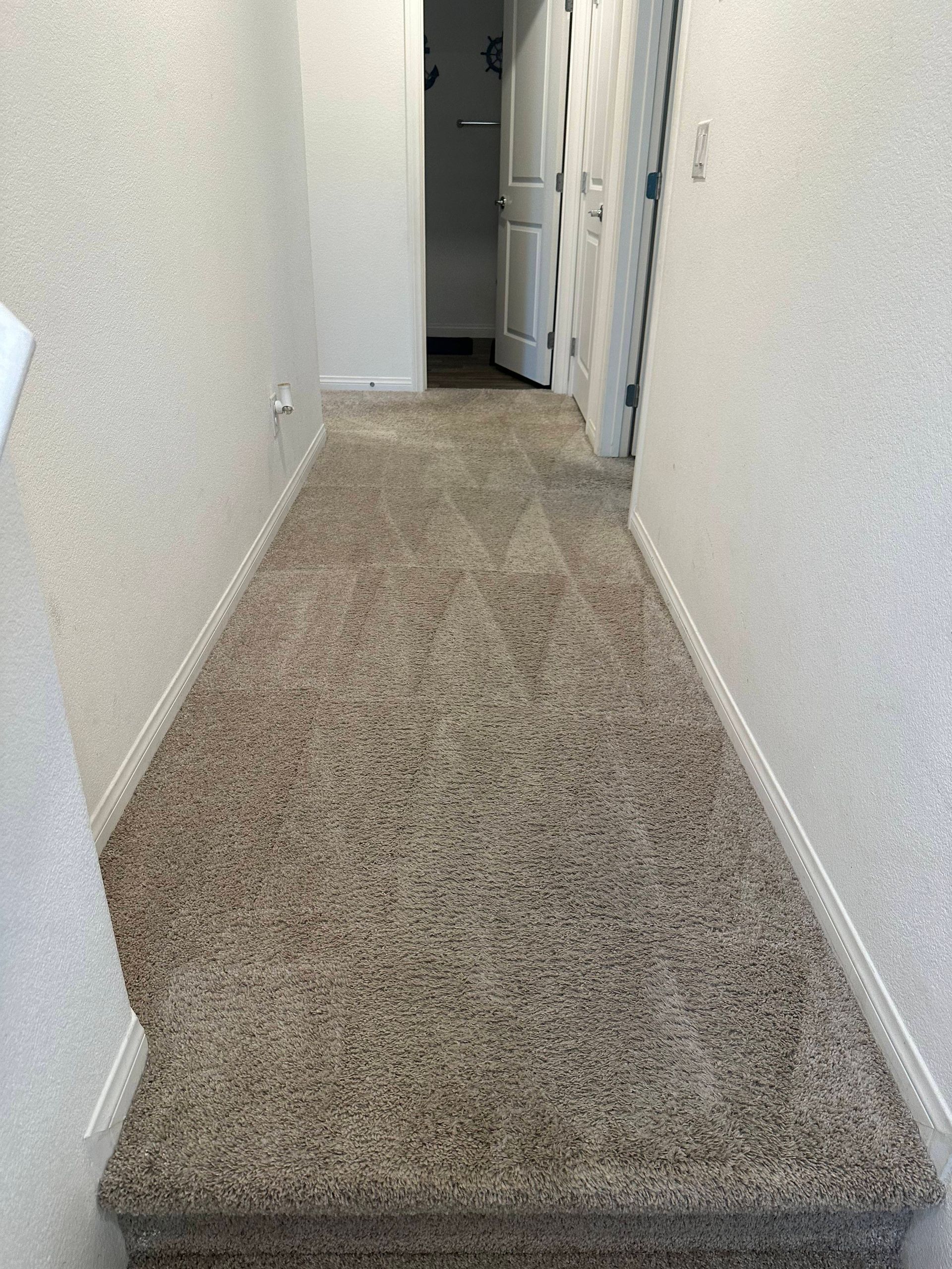 Narrow hallway with beige speckled carpet, leading to a doorway and light-colored walls.