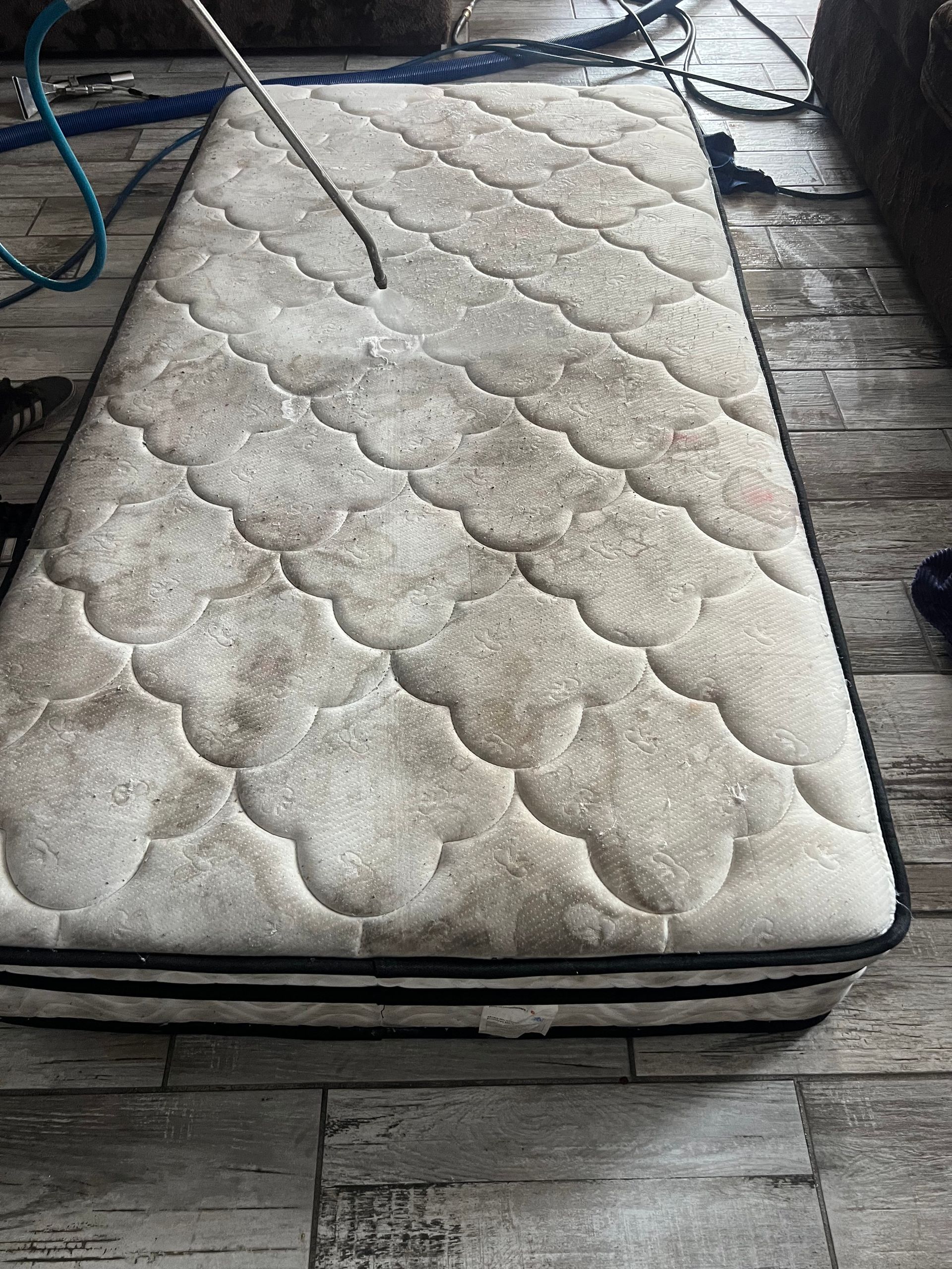 Dirty mattress being cleaned; visible dirt and stain patterns, cleaning hose present.