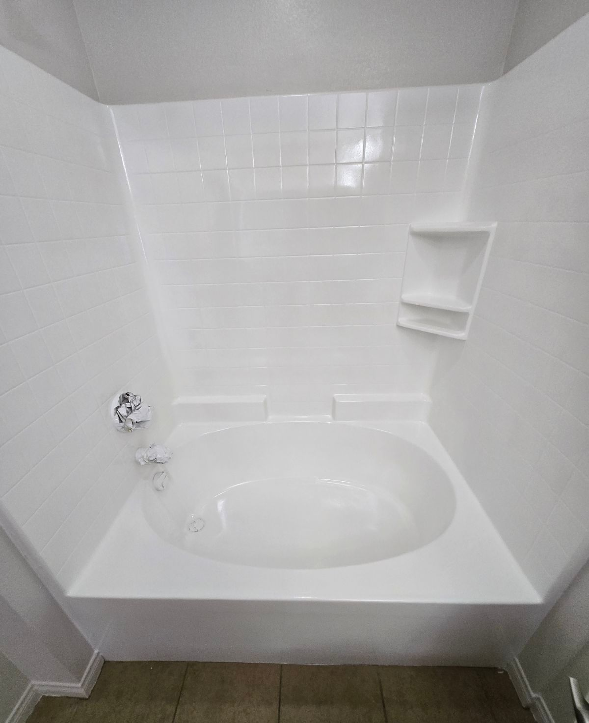A razor and toiletries on the edge of a white bathtub in a bathroom.