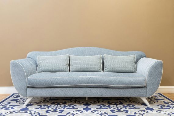Light blue sofa with patterned pillows on a blue-and-white rug against a tan wall