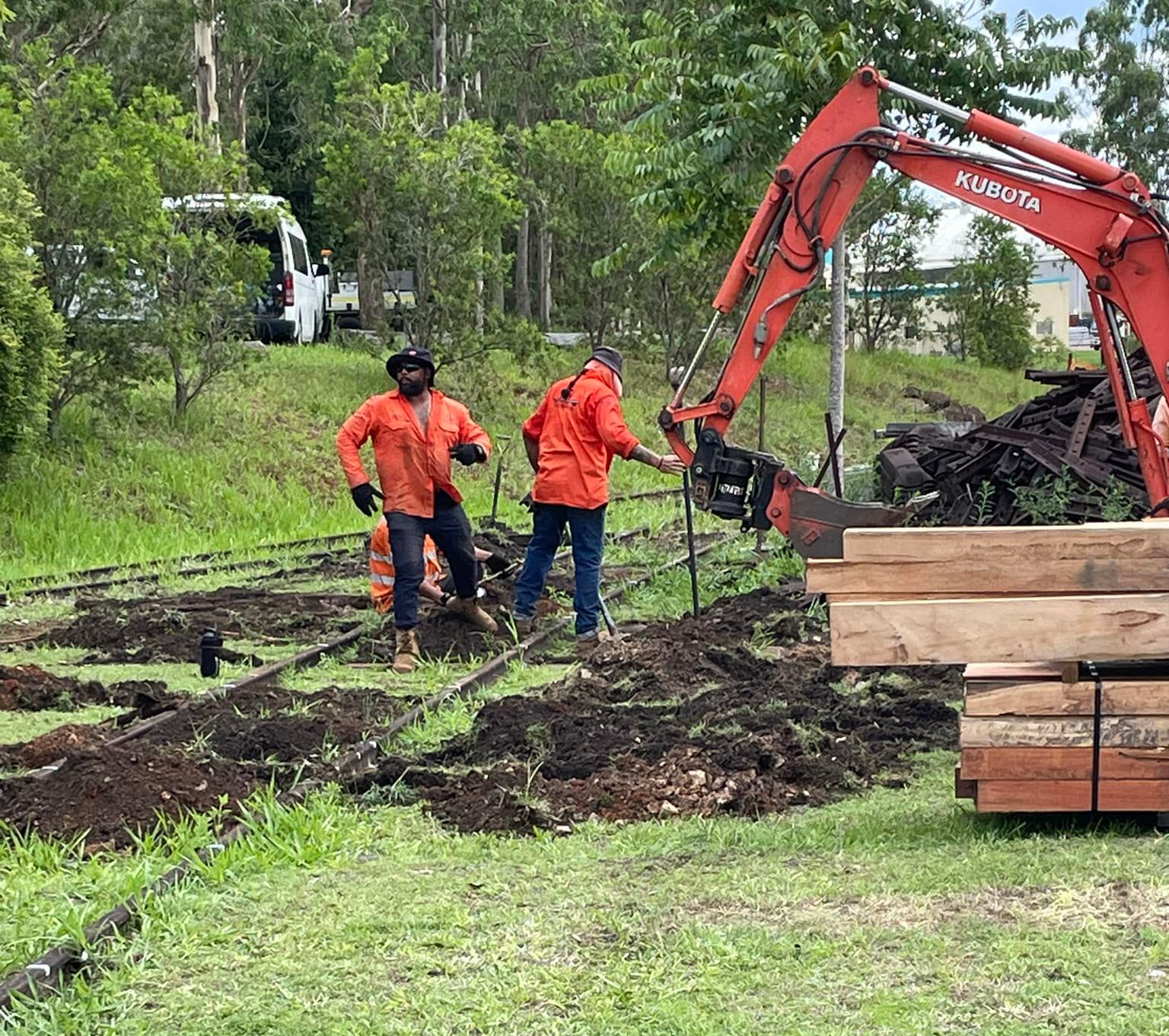 Two workers in orange vests and a red excavator are working outdoors.