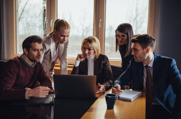 A group of people are sitting around a table looking at a laptop computer.
