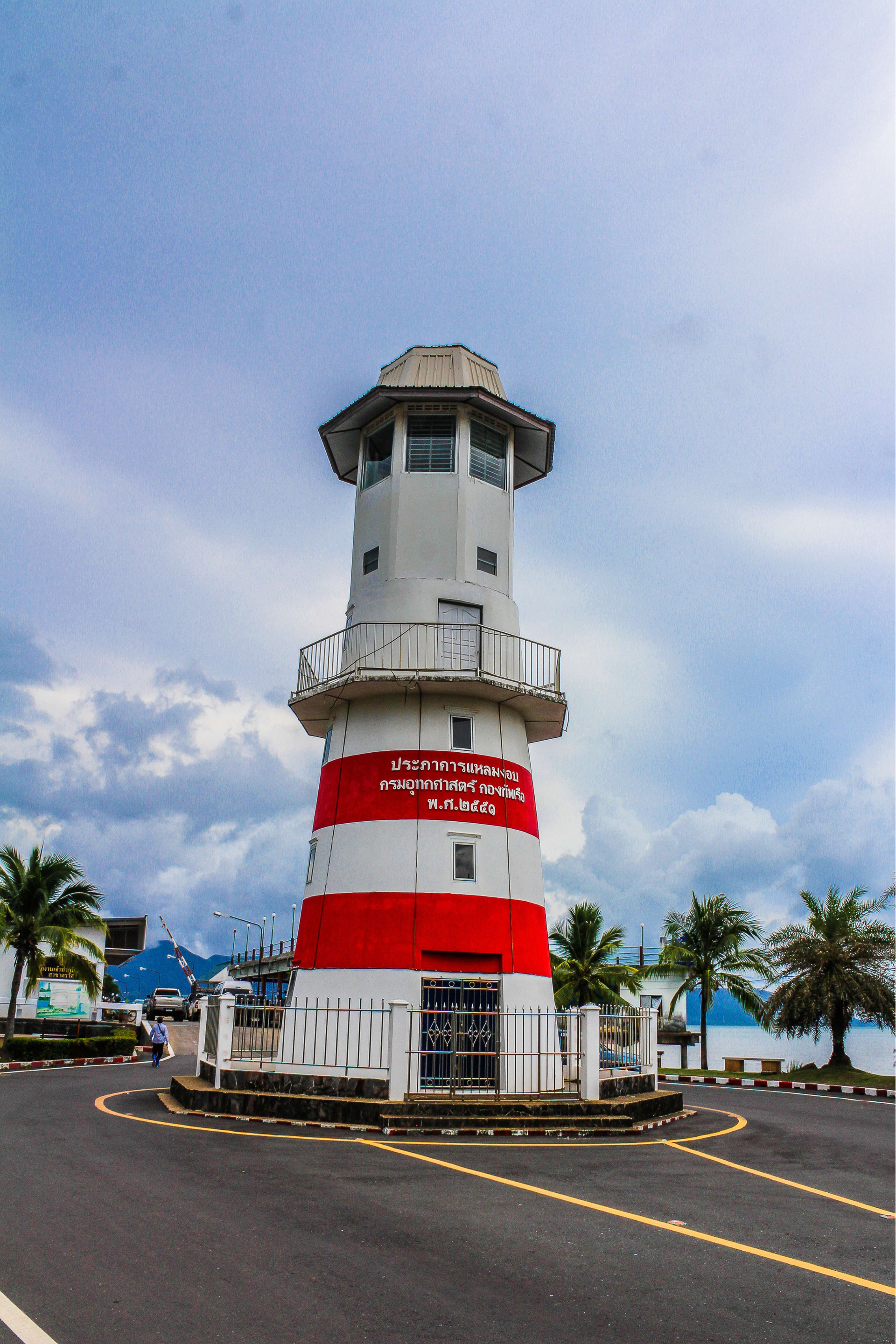 A red and white lighthouse is sitting on the side of a road.