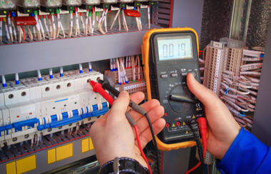 Technician testing an electrical control panel with a multimeter and red probes.