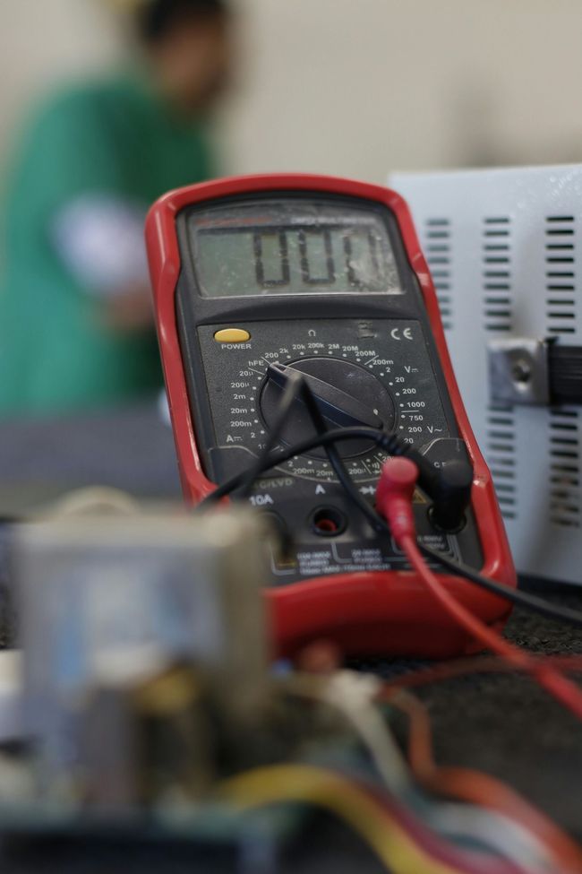 Digital multimeter with probes attached on a workbench, blurred background and circuit components nearby