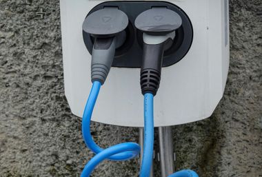 Close-up of two plugged-in cables on a white outdoor wall outlet box.