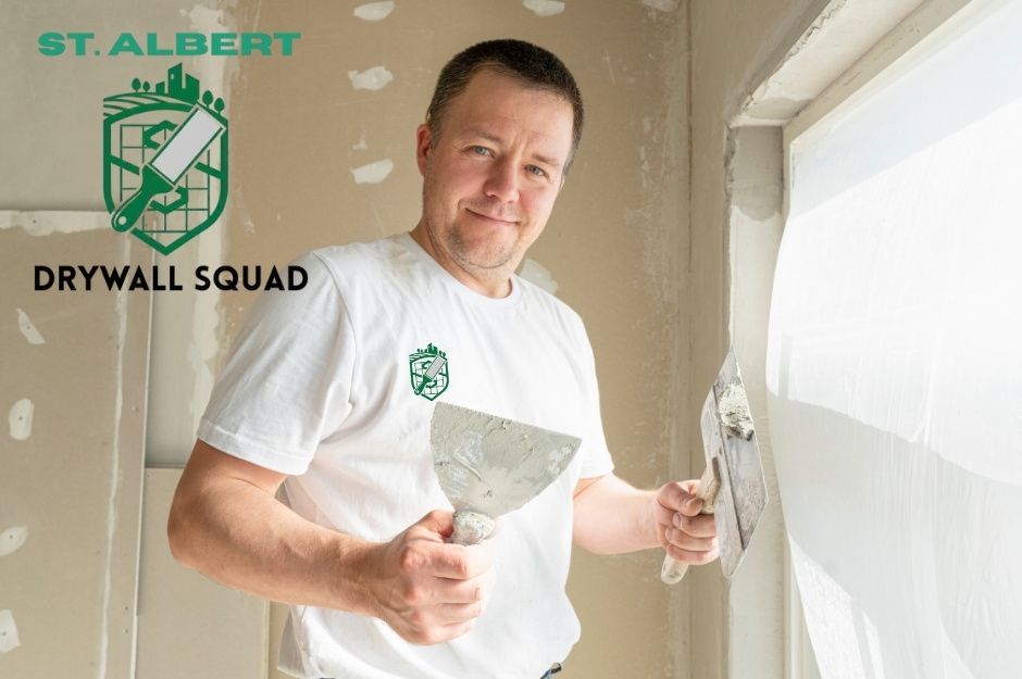 A drywall repair company professional at a commercial construction site holds a putty knife and applies joint compound to a wall. The worker wears a white t-shirt while finishing drywall in an unfinished room near Lamplight Cove, and Lamplight Dr, Spruce Grove, AB.