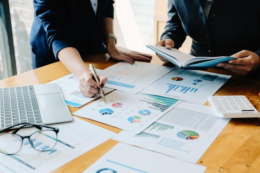 A Man and A Woman Are Sitting at A Table with Papers and A Laptop — Twin Peaks Finance In Helensvale, QLD