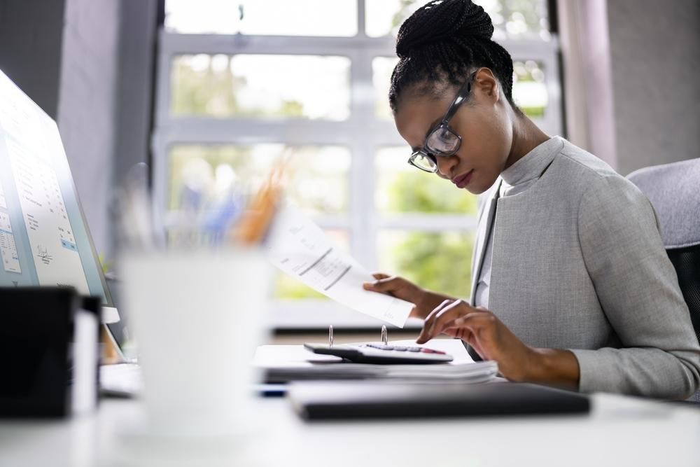 A Woman Is Sitting at A Desk with A Calculator and A Piece of Paper — Twin Peaks Finance In Helensvale, QLD
