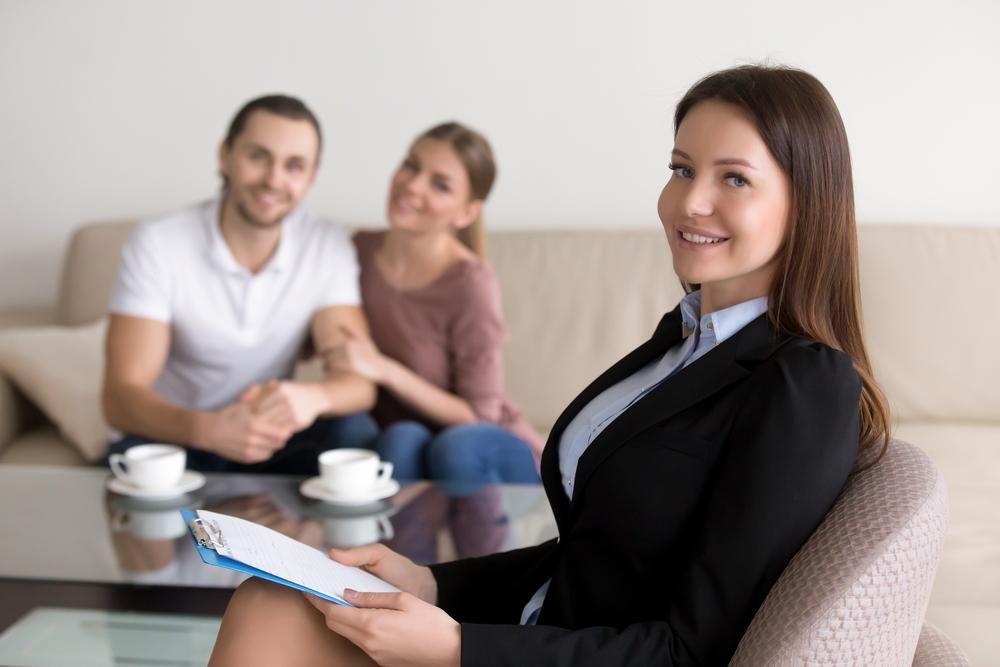 A Woman Is Sitting in A Chair with A Clipboard in Front of A Couple — Twin Peaks Finance In Helensvale, QLD