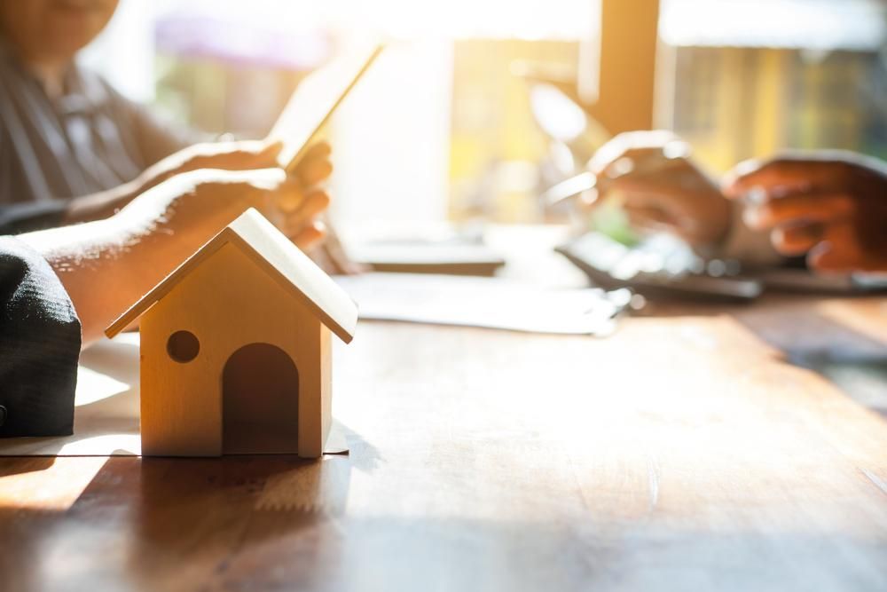 A Small Model House Is Sitting on A Wooden Table Next to A Person Using a Tablet — Twin Peaks Finance In Helensvale, QLD