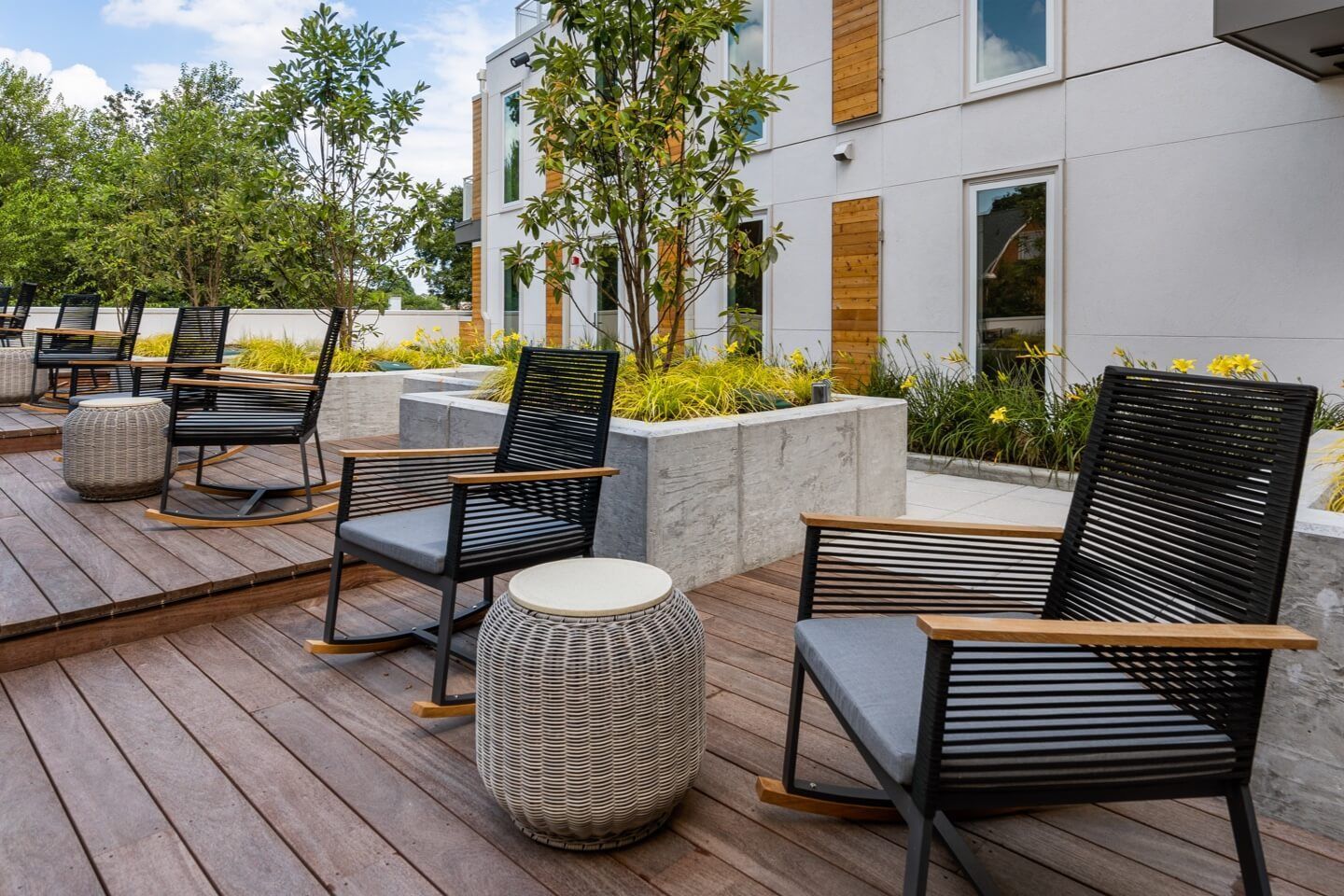 A wooden deck with rocking chairs and tables on it.