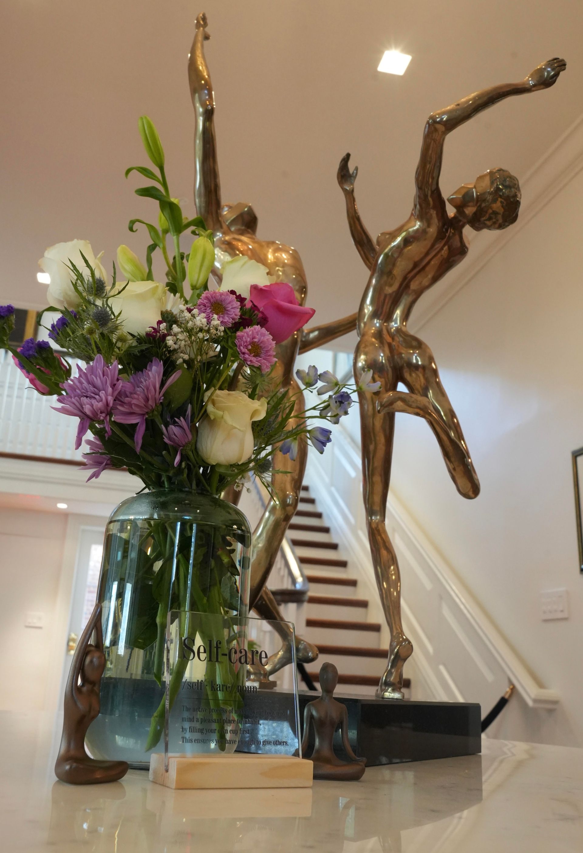 Bronze ballerina sculptures with flower bouquet, white staircase background.