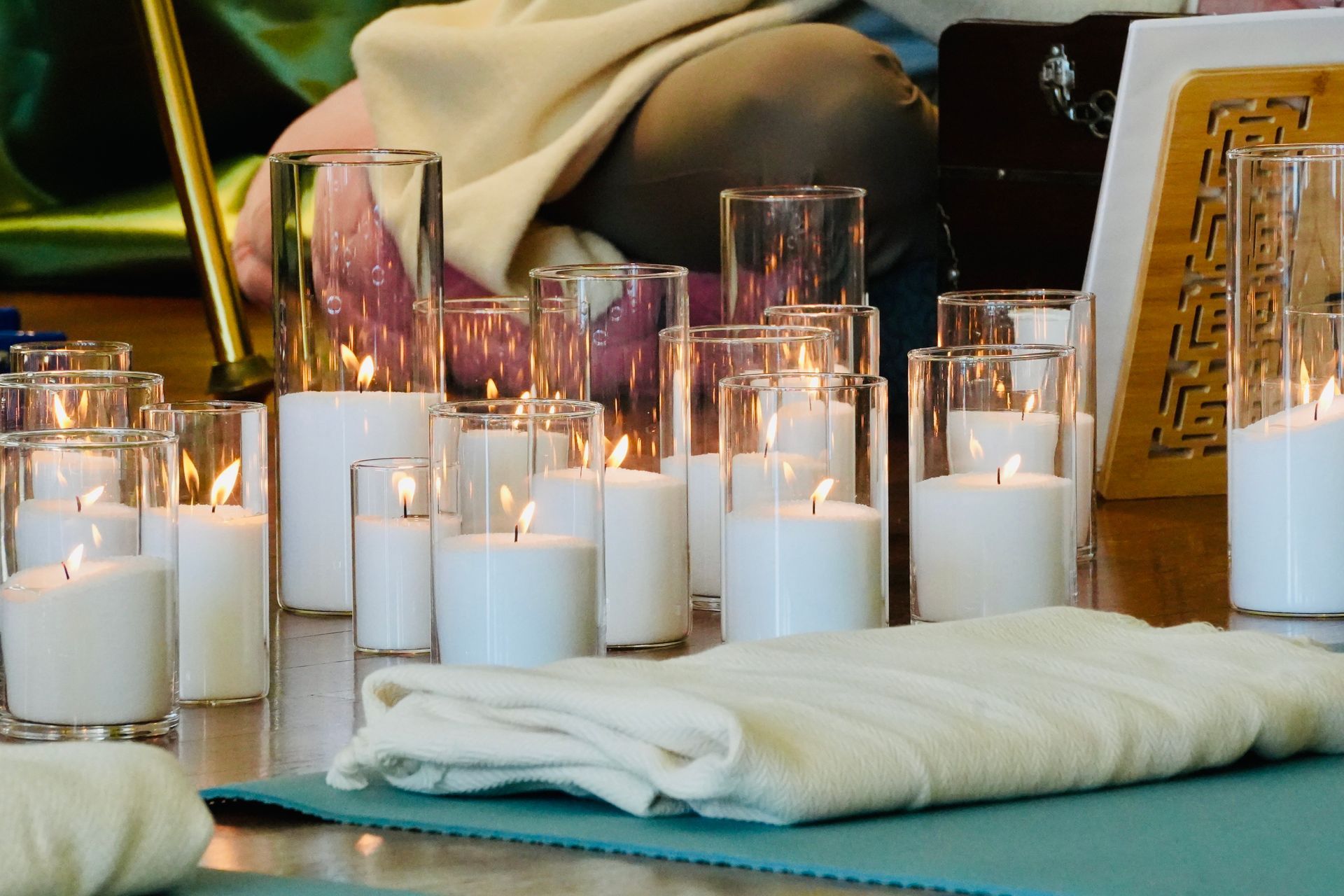 Lit candles in glass cylinders and on a table; cloth and blue mat in foreground.