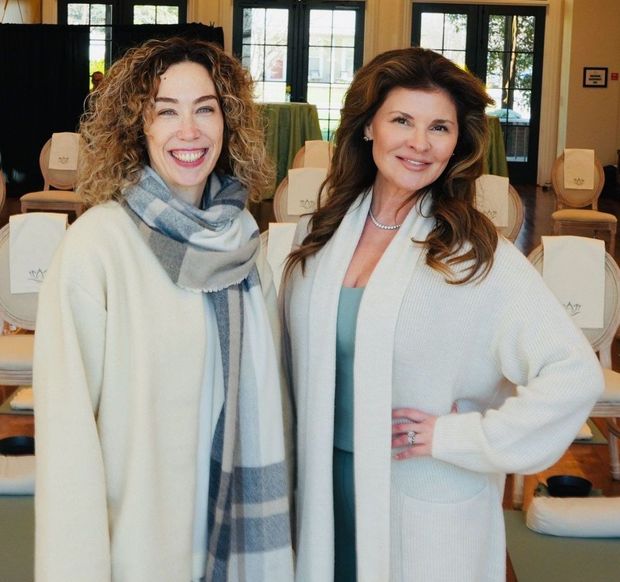 Two smiling women pose in a bright room with singing bowls. One wears a scarf, the other a cardigan.