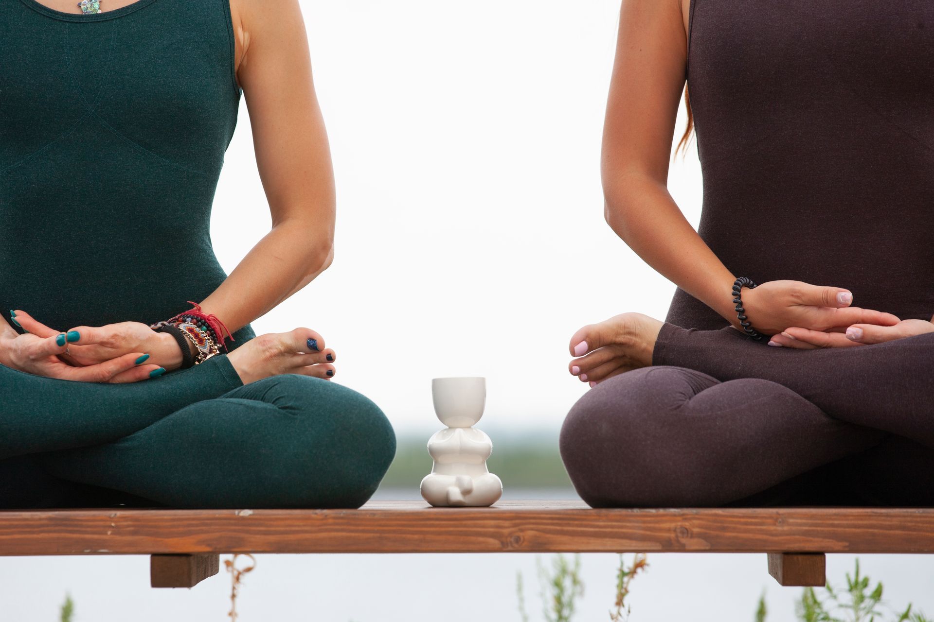 Two women are sitting in a lotus position on a wooden bench.