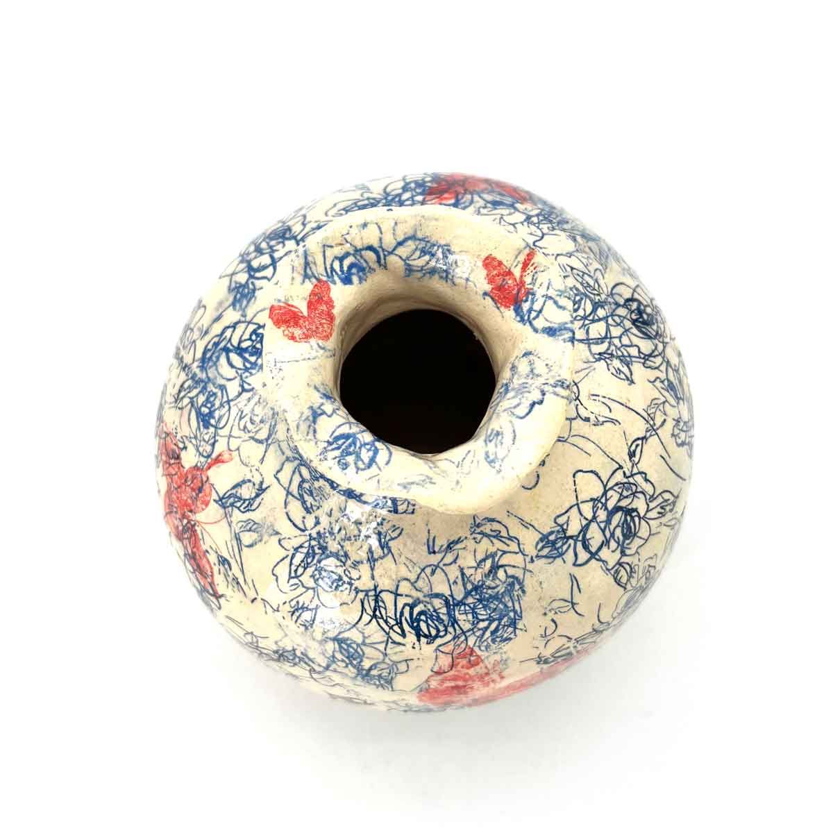 Bovenaanzicht van een crèmekleurige keramische vaas met blauw craquelépatroon en rode accenten.