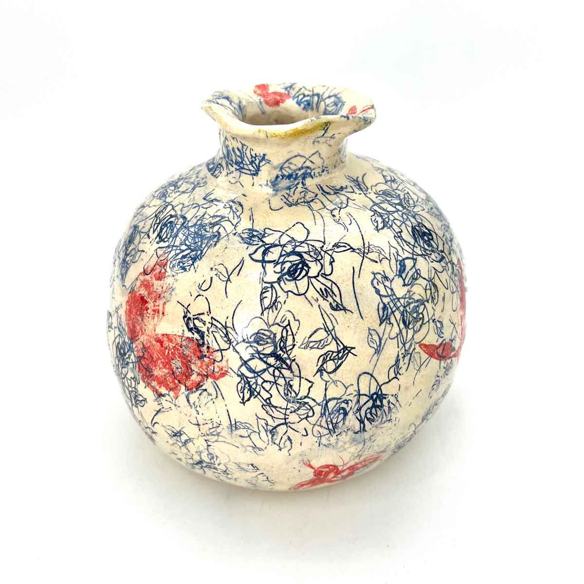 Ronde keramische vaas met een blauw bloemenpatroon en rode accenten op een witte achtergrond.