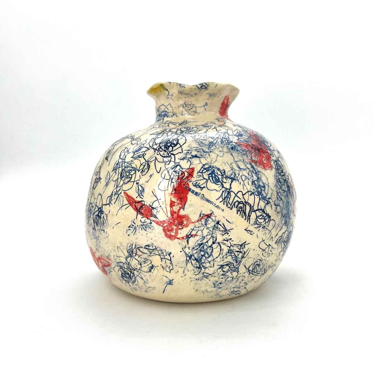 Klein crèmekleurig keramisch vaasje met blauwe en rode abstracte patronen op een witte achtergrond.