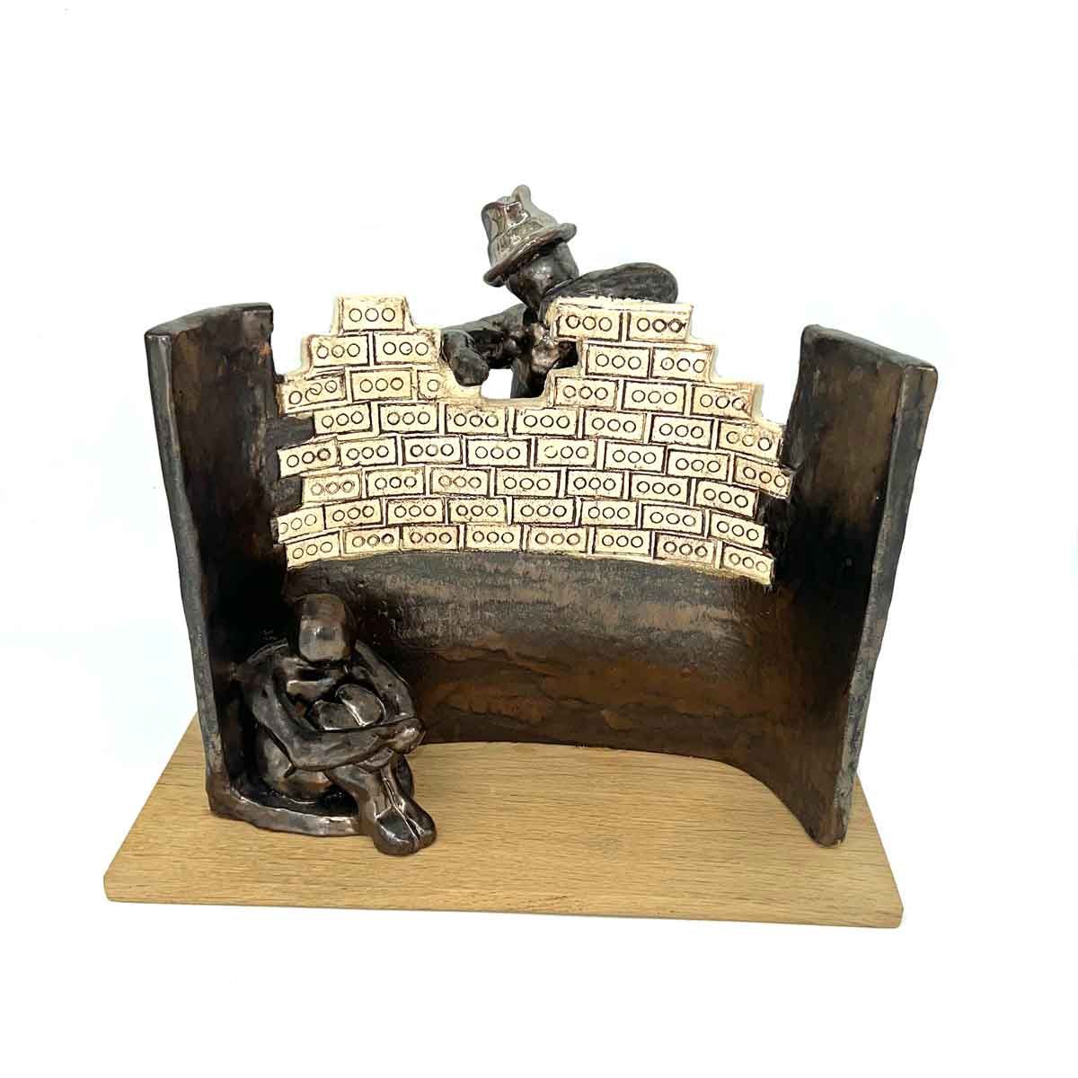 Een klein beeldje van een bakstenen muur met daaronder een zittende figuur en een andere figuur die over de rand heen gluurt.