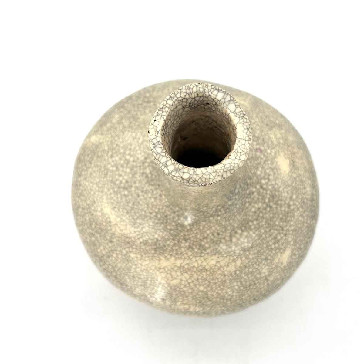 Klein beige keramisch vaasje met een ronde vorm en een smalle opening, afgebeeld op een witte achtergrond.