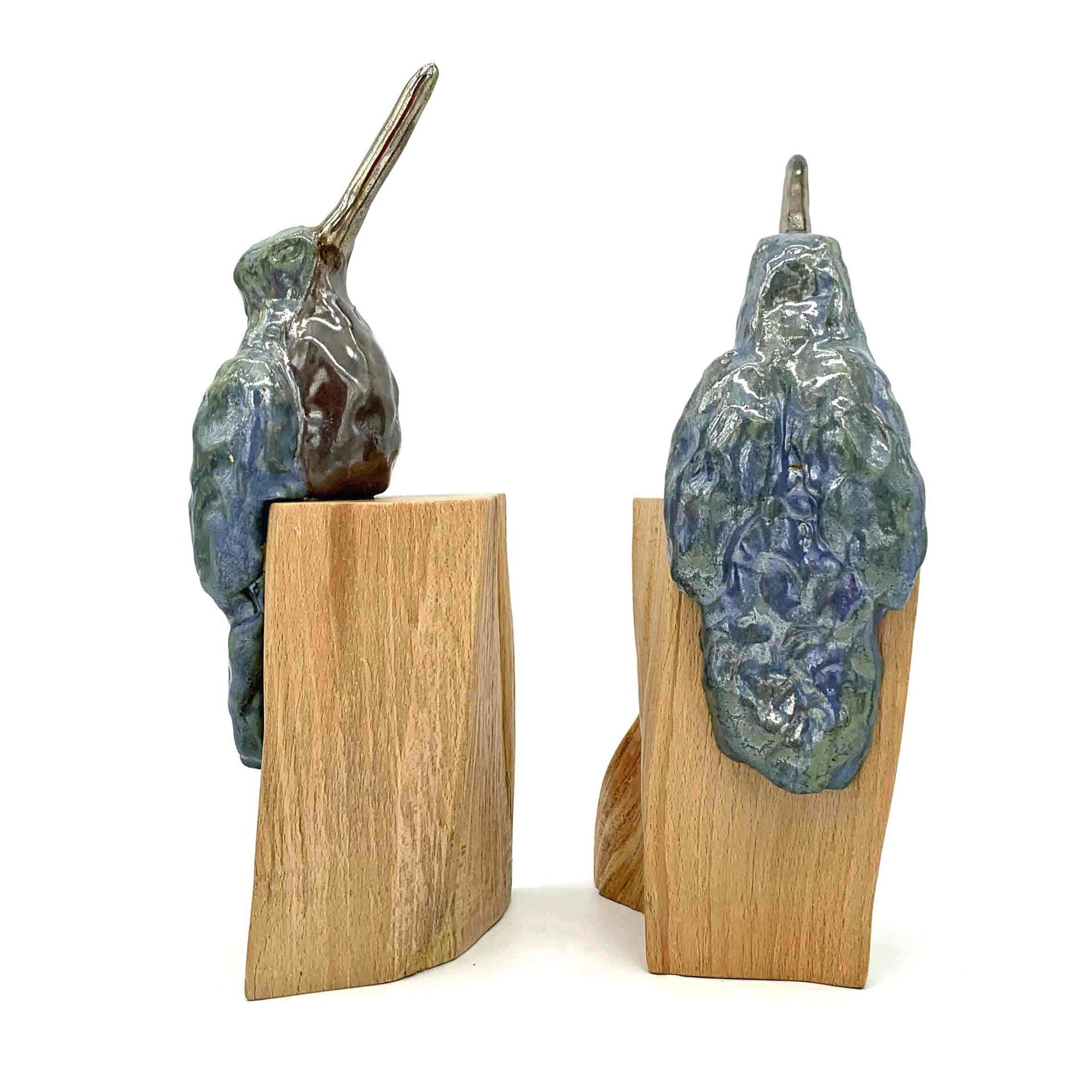 Twee kleine blauwgrijze sculpturen, gemonteerd op houten blokken, elk met een hoornachtig uitsteeksel.