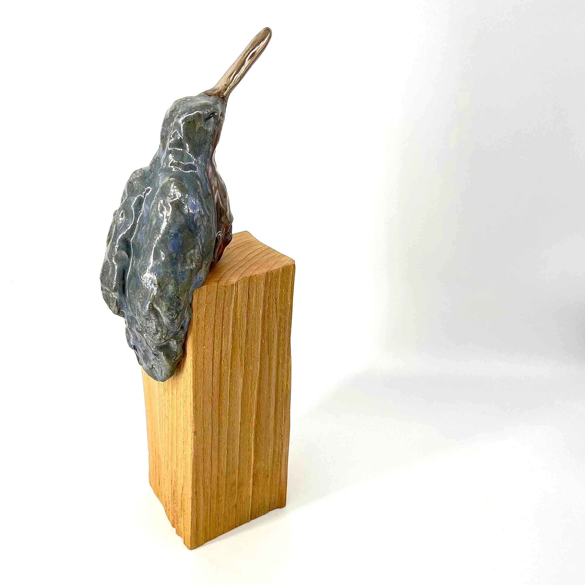 Klein donkermetalen vogelbeeldje, zittend op een houten blokje tegen een witte achtergrond.