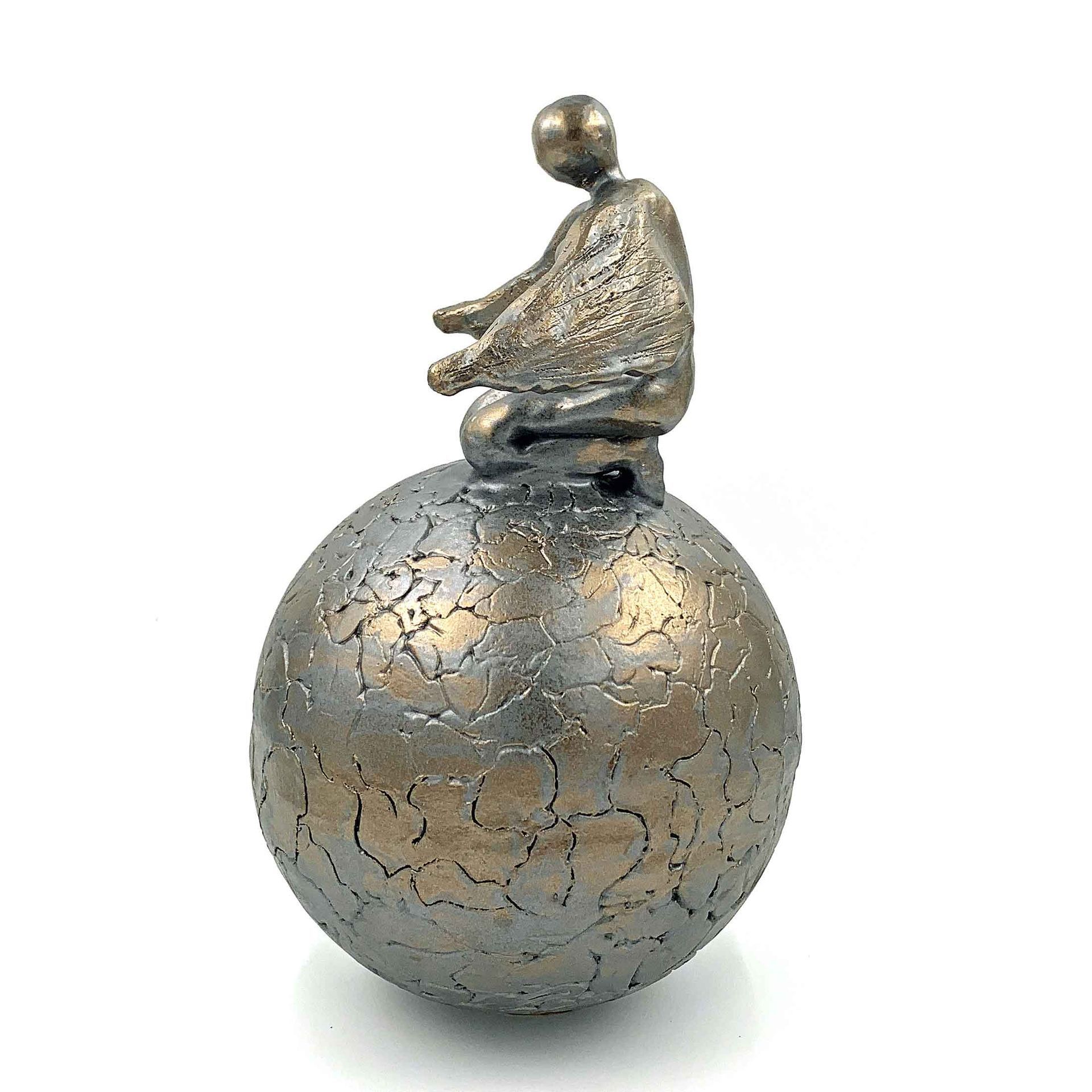 Klein bronzen zittend beeldje bovenop een gebarsten metalen bolsculptuur