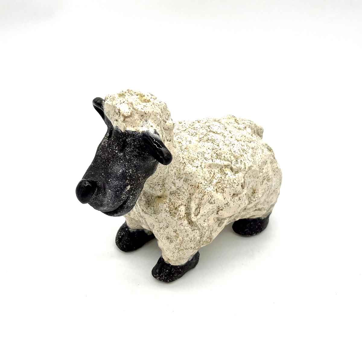Klein decoratief schaapje met een zwart gezicht en zwarte poten op een witte achtergrond.