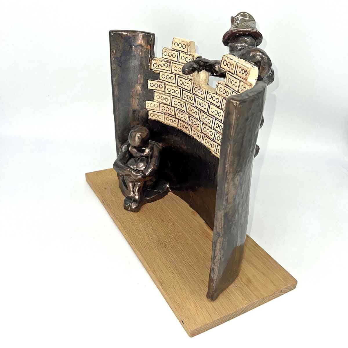 Klein, uit hout gesneden beeldje op een sokkel, met twee zittende figuren en een gedecoreerde boog.