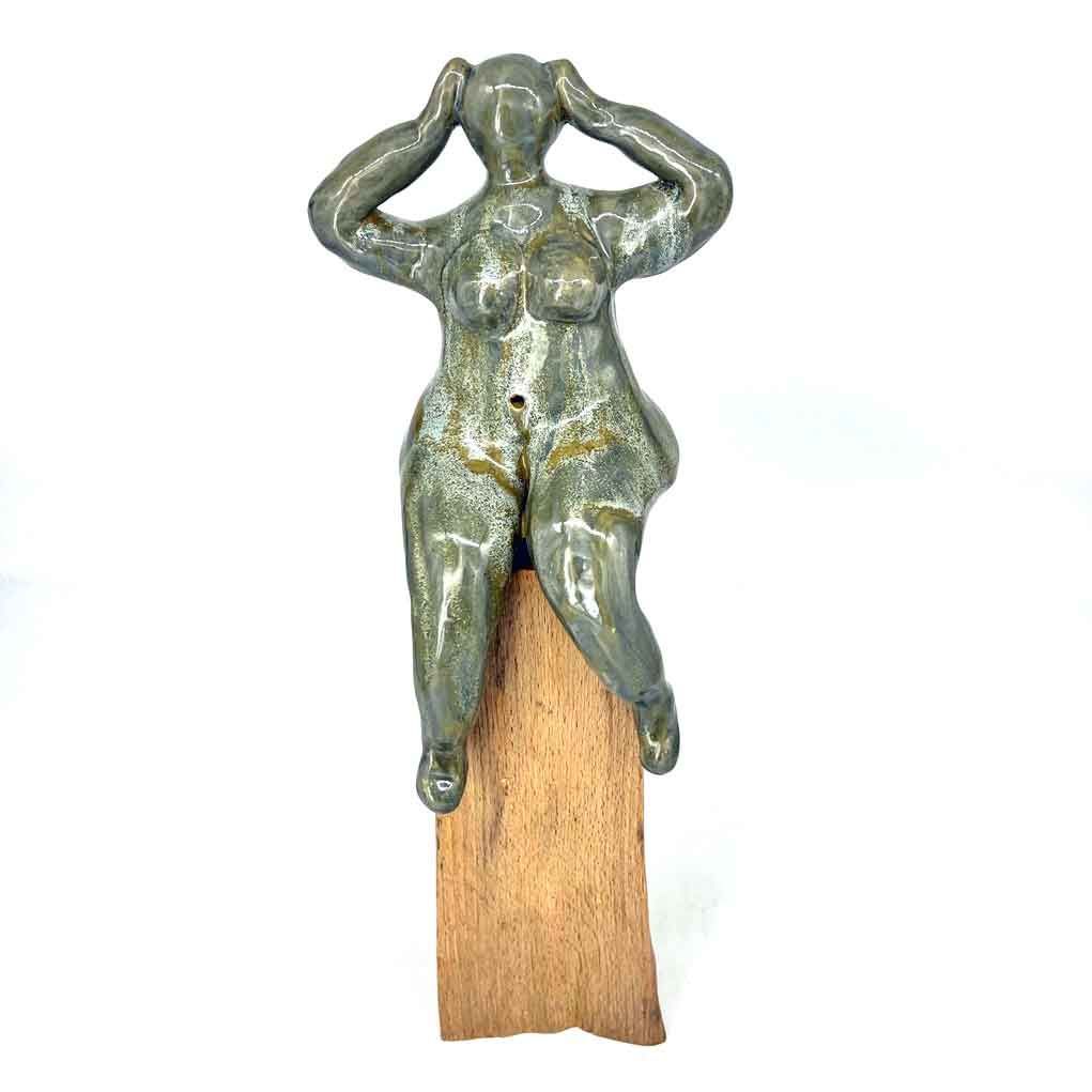 Klein, groenachtig metalen beeldje met handen op het hoofd, zittend op een houten voetstuk.
