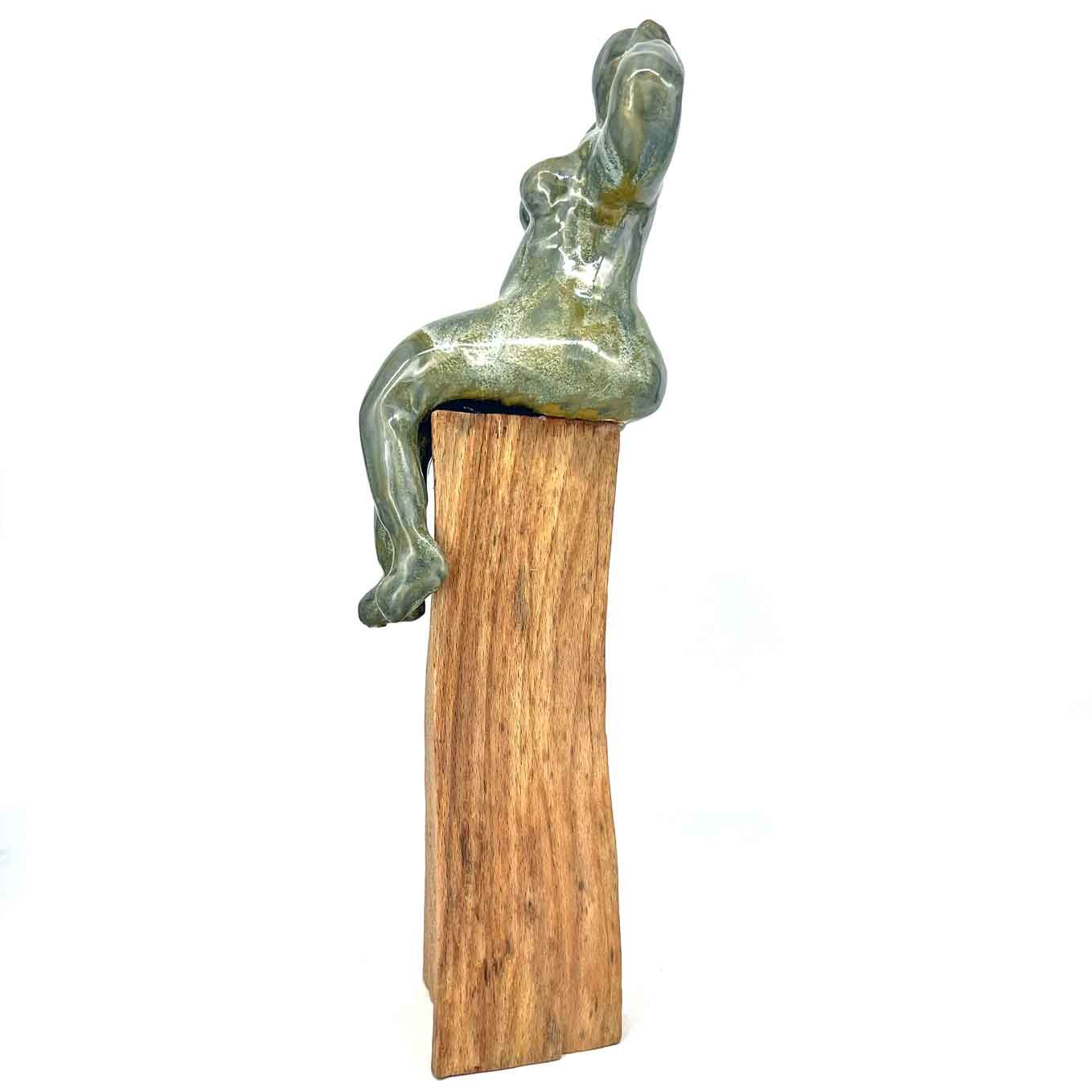 Groenachtig abstract figuurtje, zittend op een verticaal houten blok, geïsoleerd op een witte achtergrond.
