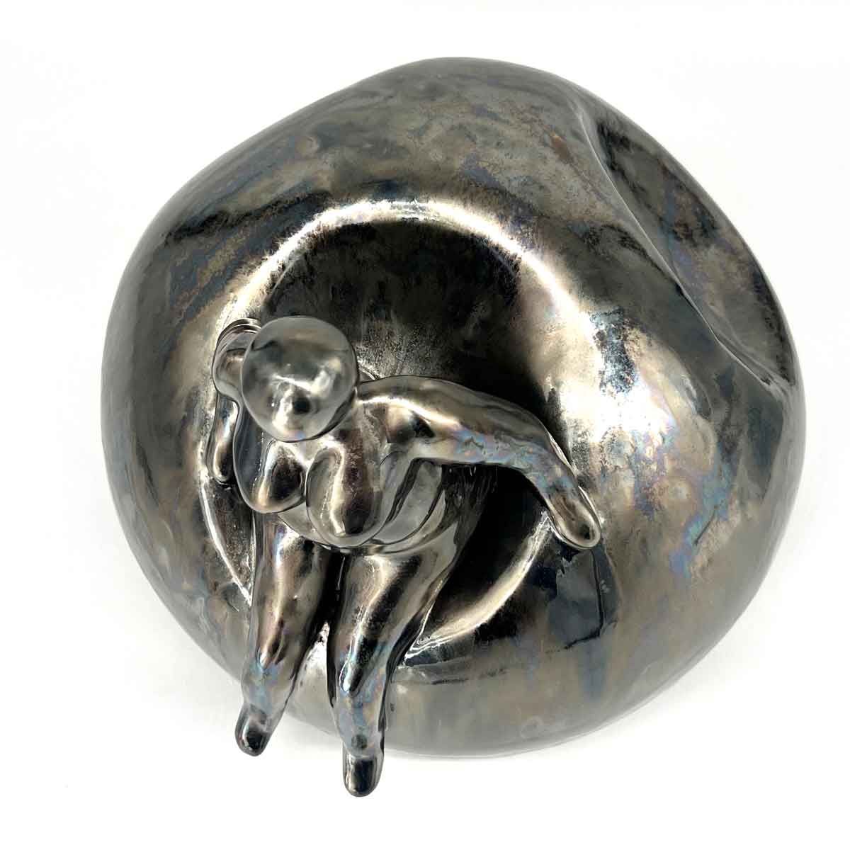 Zilveren sculptuur van een zittende menselijke figuur, opgerold in een afgeronde, metalen vorm.