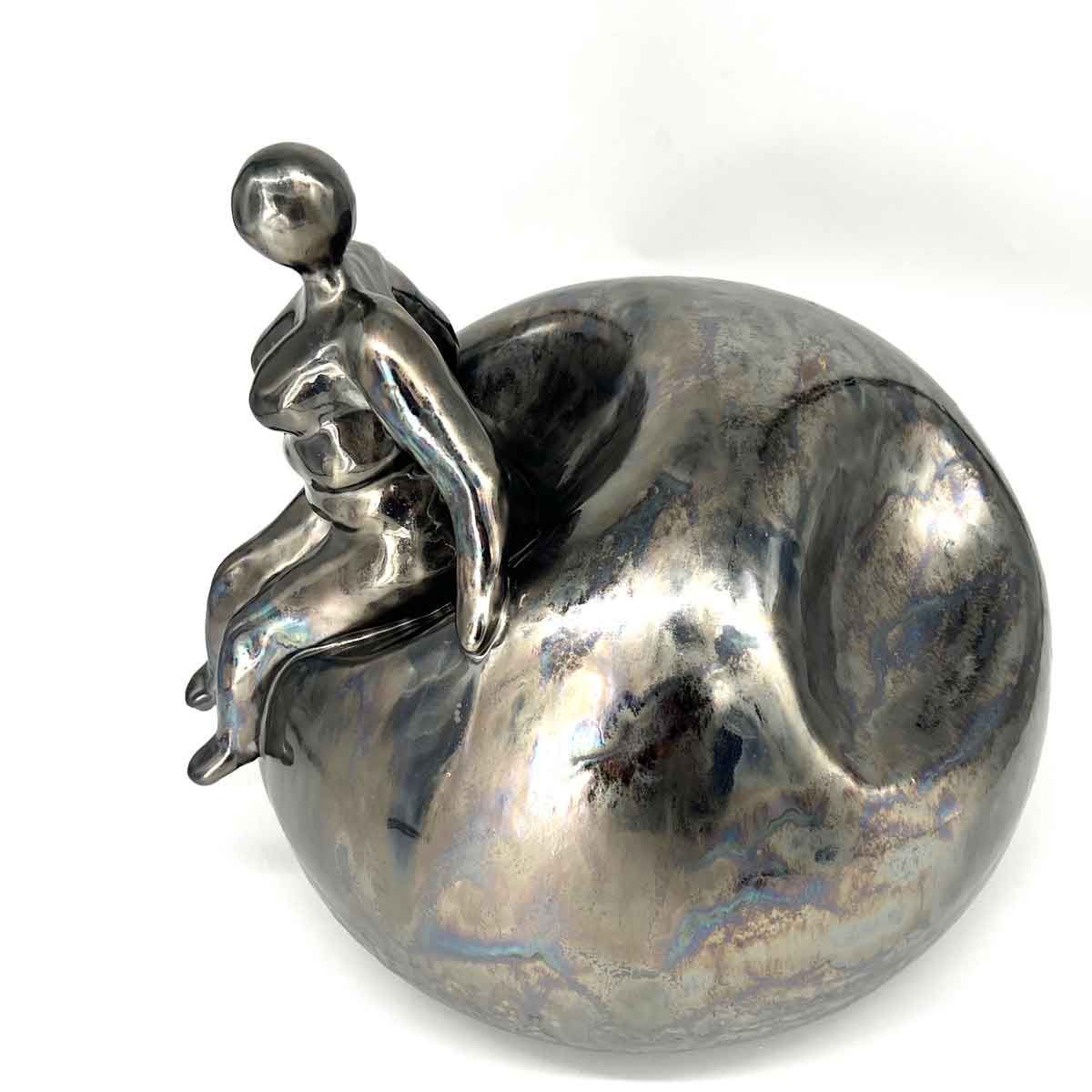 Klein zilveren beeldje van een zittend persoon op een glanzende metalen bol.