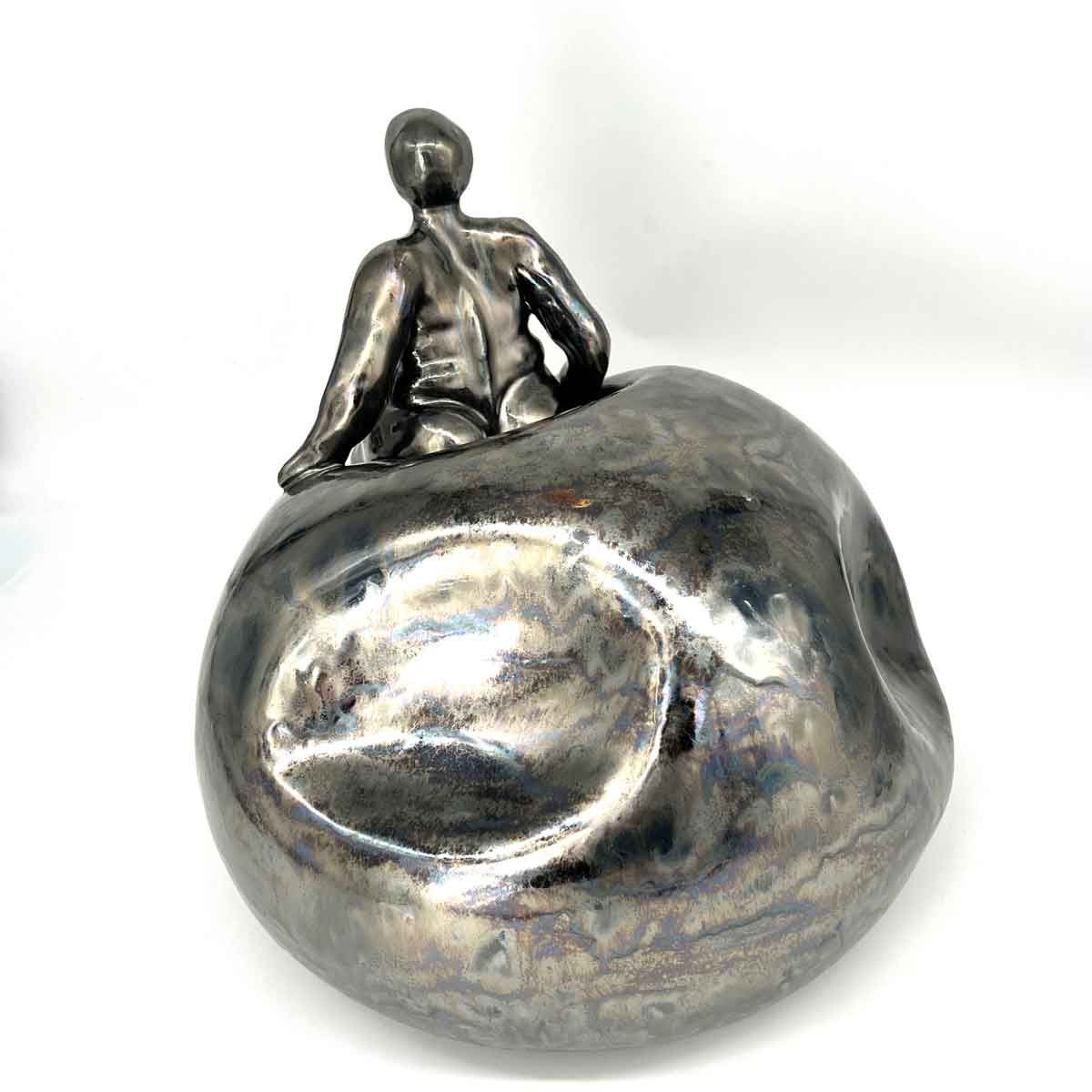 Klein zilveren beeldje van een zittende persoon op een afgeronde metalen voet.