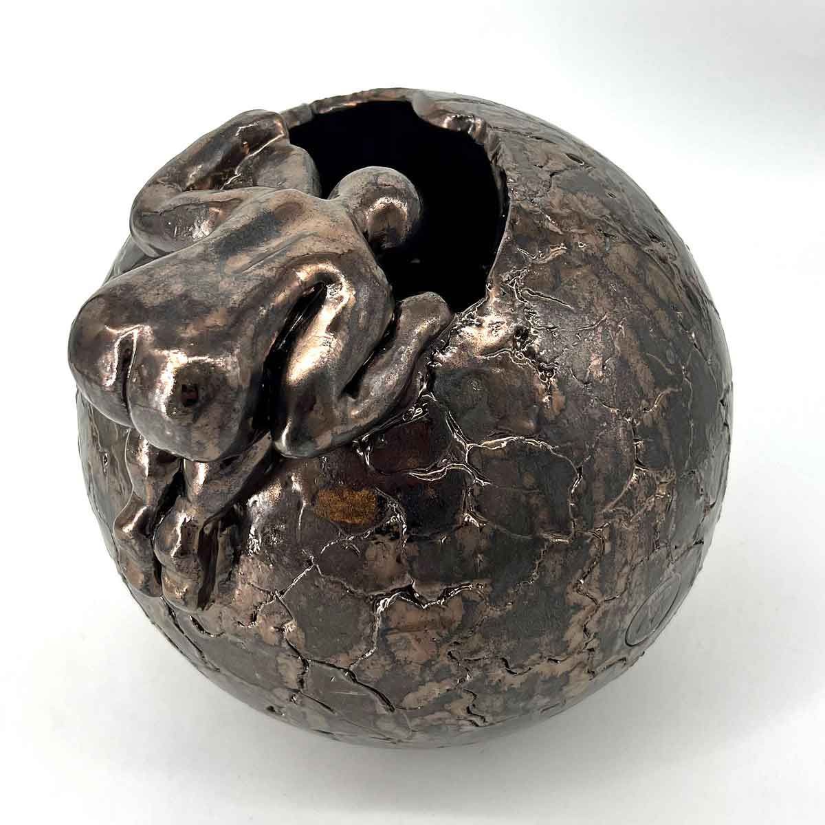 Bronzen sculptuur van een klein wezentje dat vanuit een gebarsten bol naar buiten gluurt.