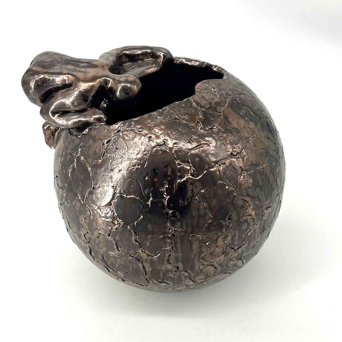 Klein, donkermetalen beeldje van een appel met een blad op een witte achtergrond.