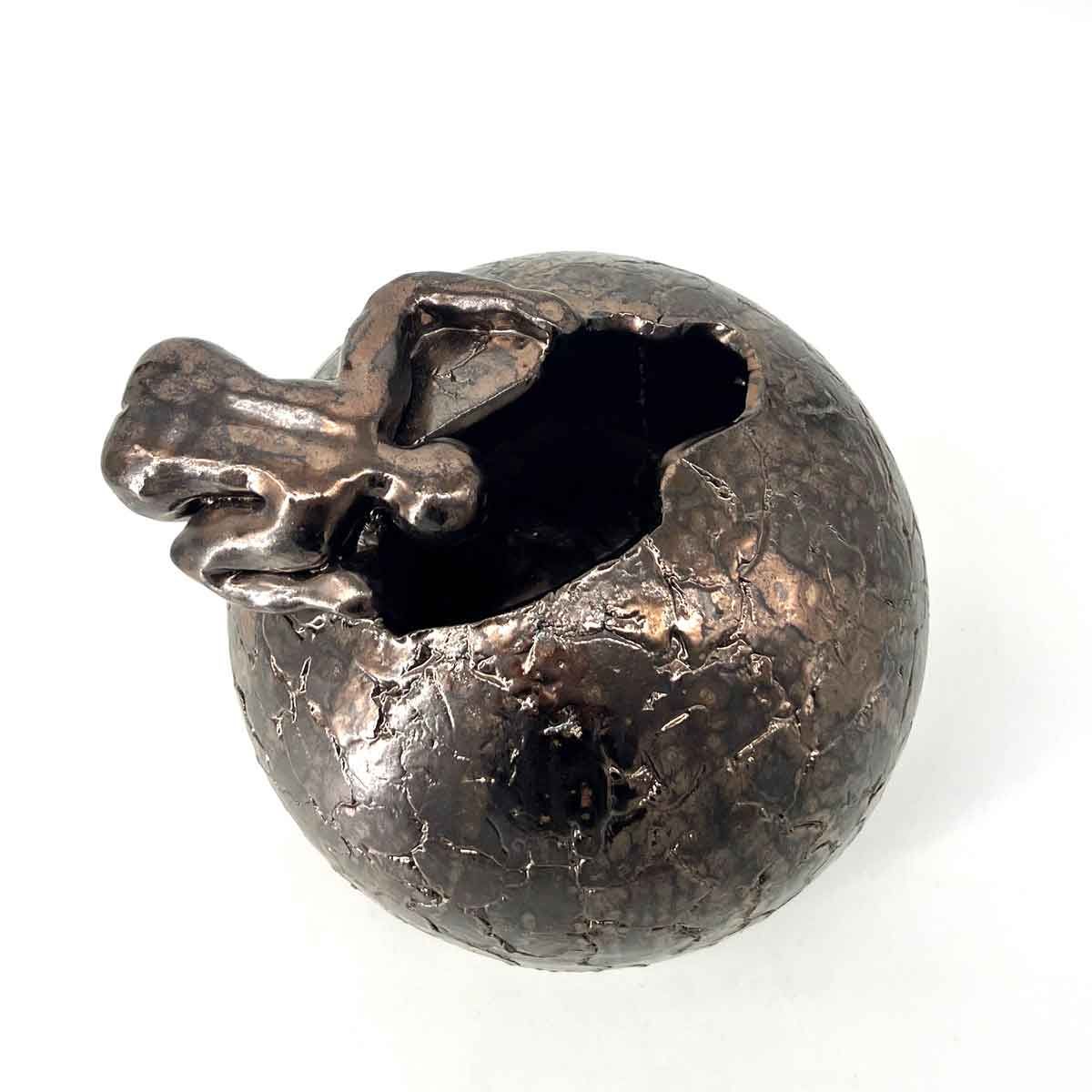 Beschadigd donkermetalen bolvormig object met een gebroken opening en een uitstekend kruisvormig stuk.