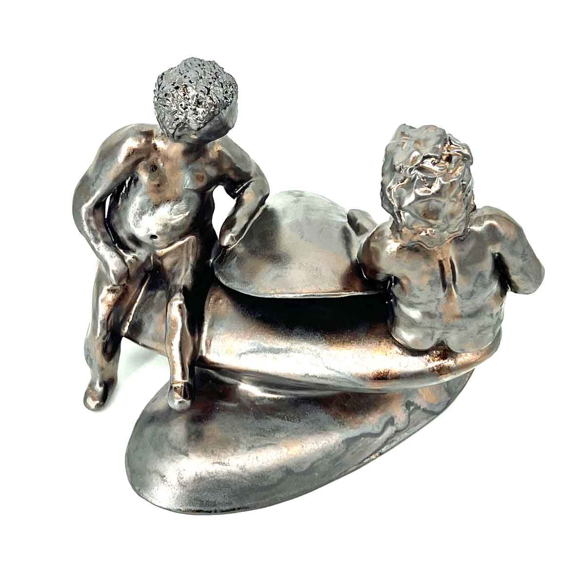 Klein zilveren beeldje van twee zittende personen op een gebogen metalen voet.