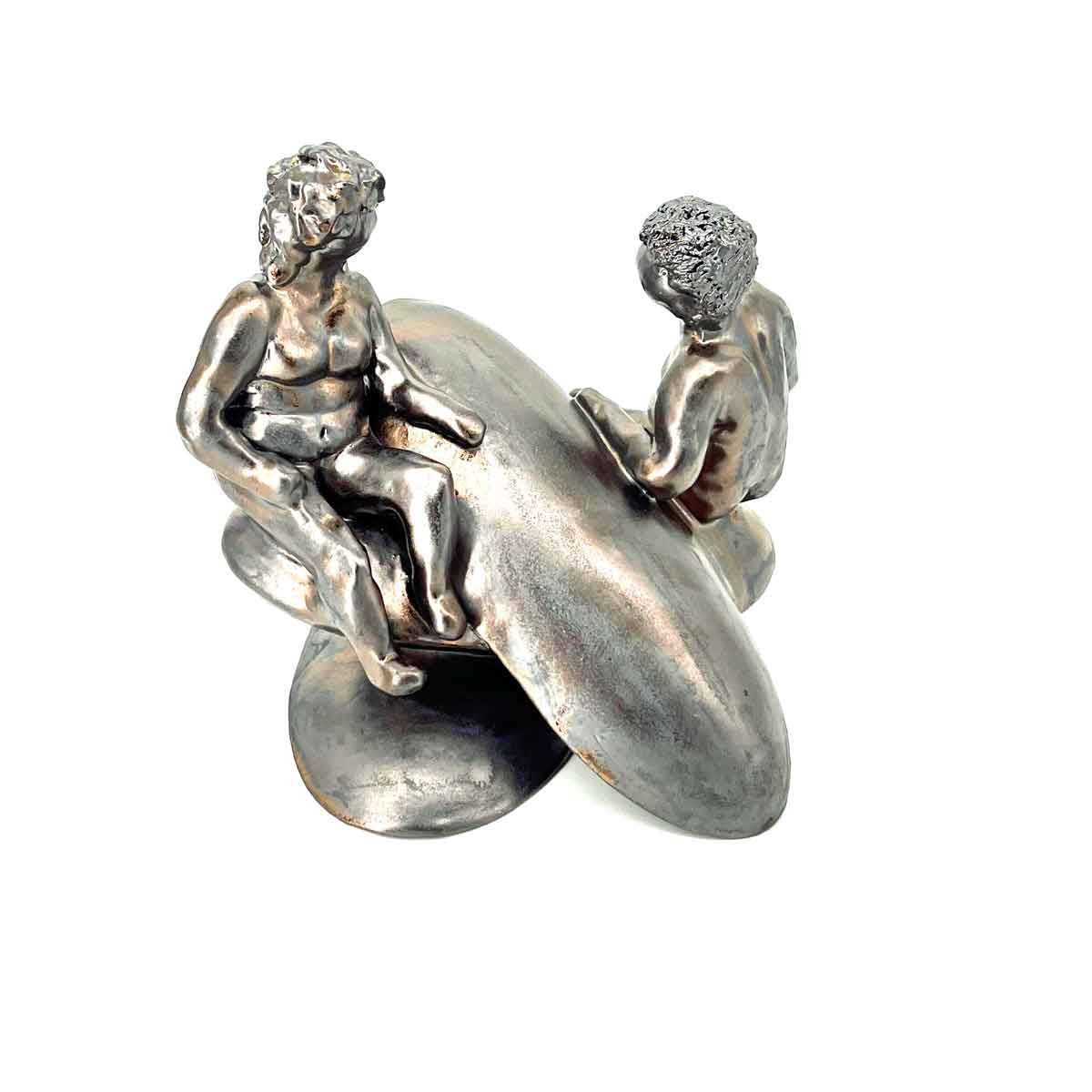 Twee kleine zilveren beeldjes zitten op een glanzende abstracte sculptuur tegen een witte achtergrond.