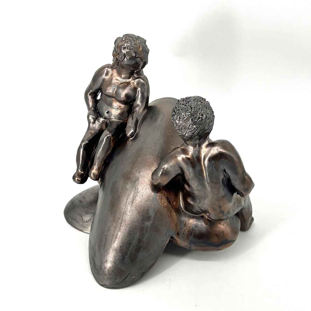 Twee kleine bronzen beeldjes zitten op een gebogen metalen vorm tegen een witte achtergrond.