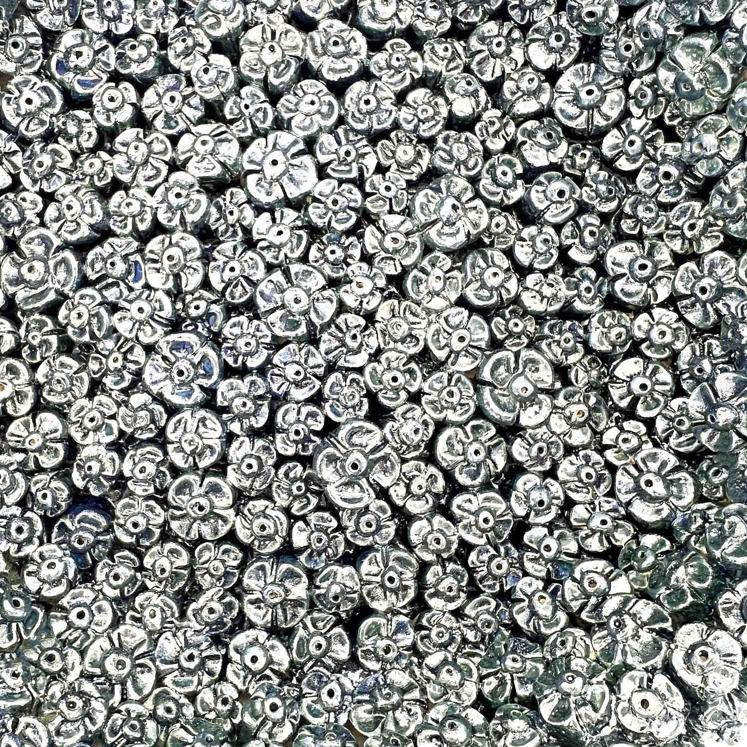 Close-up van een dichte cluster van kleine zilverkleurige metalen kralen of korrels, die het hele beeldvlak vullen.