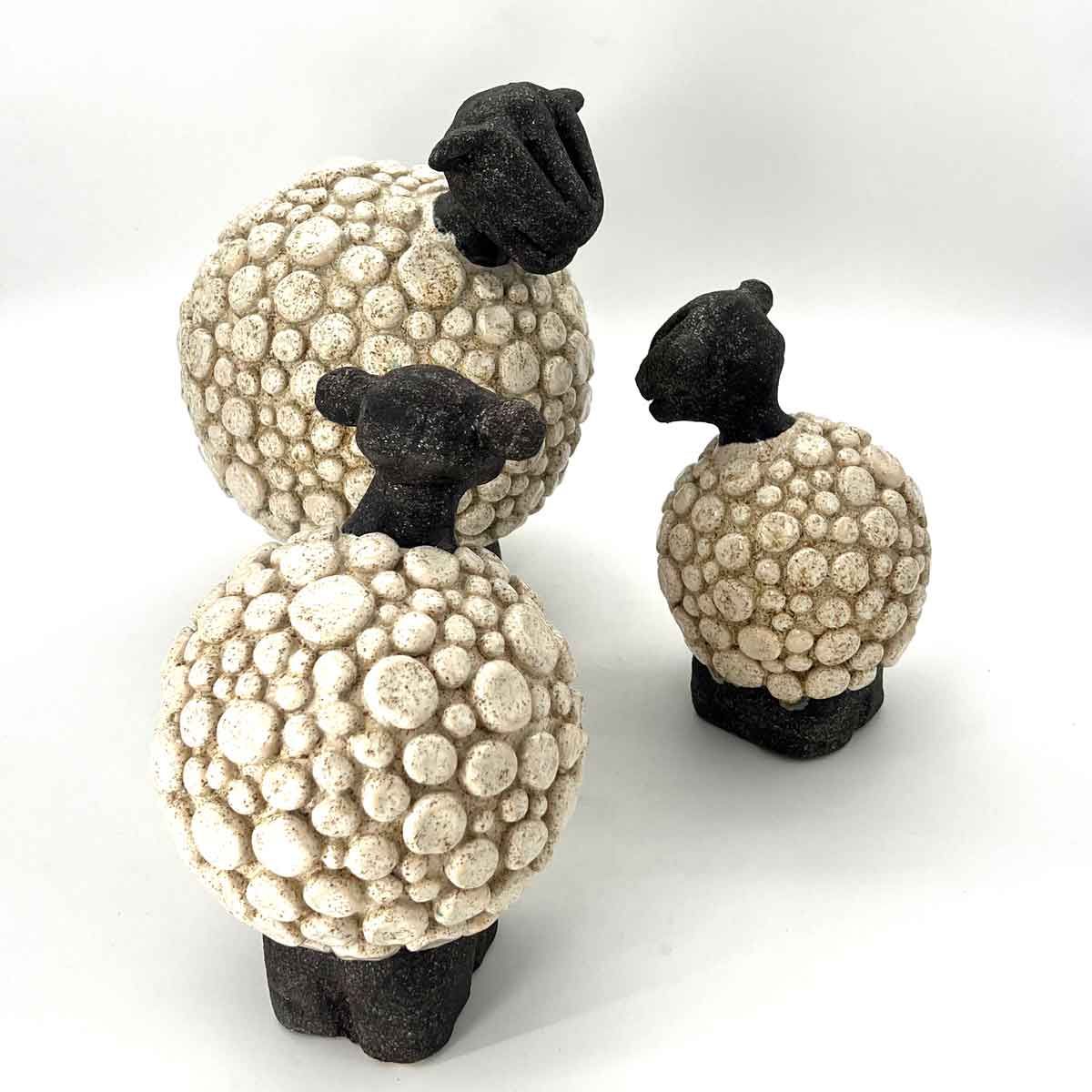Drie kleine schaapjesfiguurtjes met witte, gestructureerde lijfjes en zwarte kopjes op een witte achtergrond.