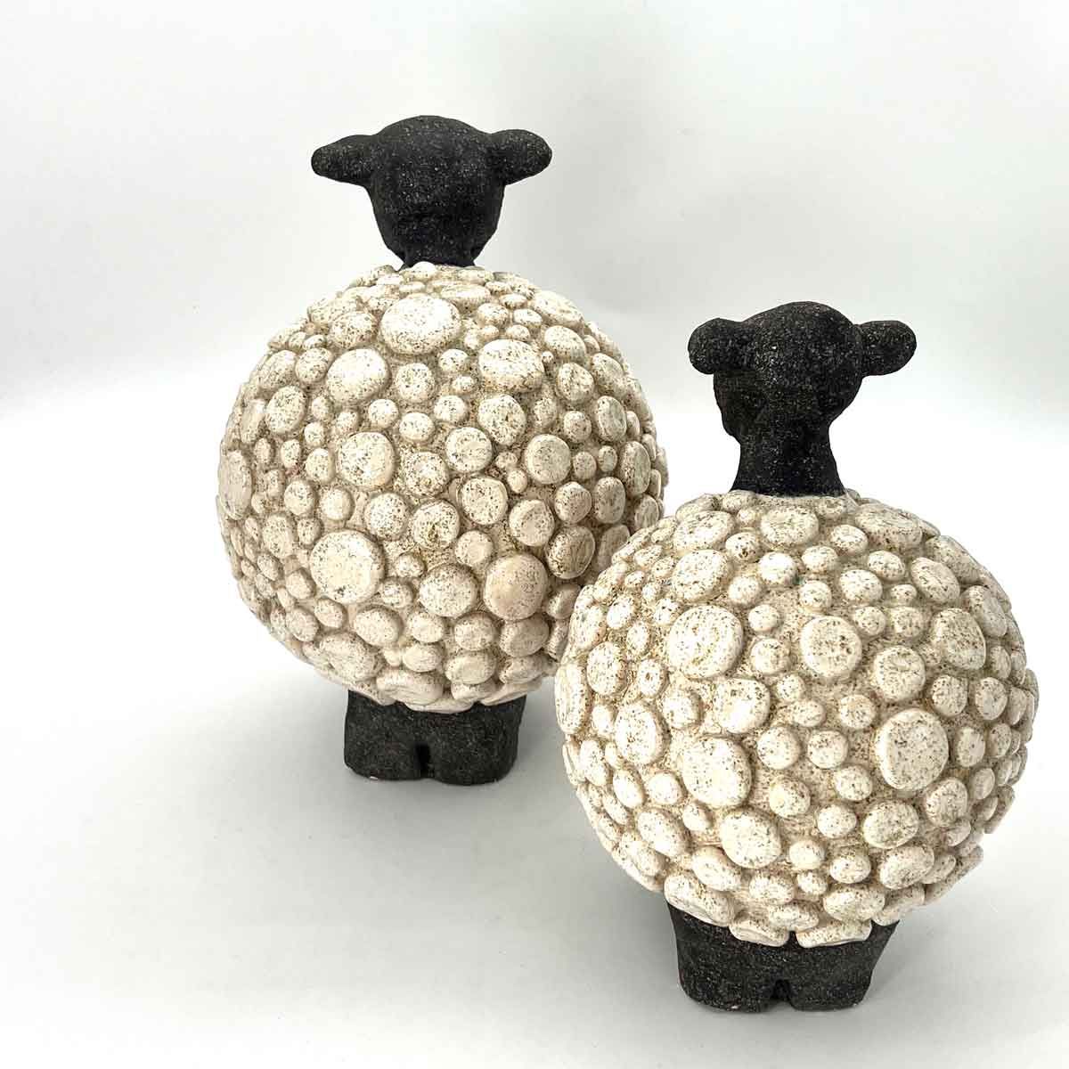 Twee schapenfiguurtjes met witte, gestructureerde wol en zwarte koppen en poten op een witte achtergrond.