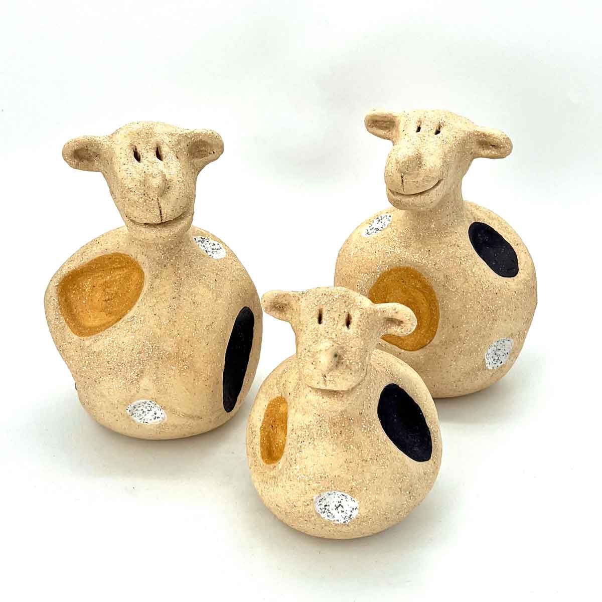 Drie crèmekleurige schaapjes met gespikkelde vlekjes op een witte achtergrond.
