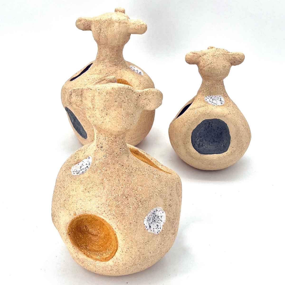 Drie beige keramische flessen met ronde, gekleurde openingen op een witte achtergrond.