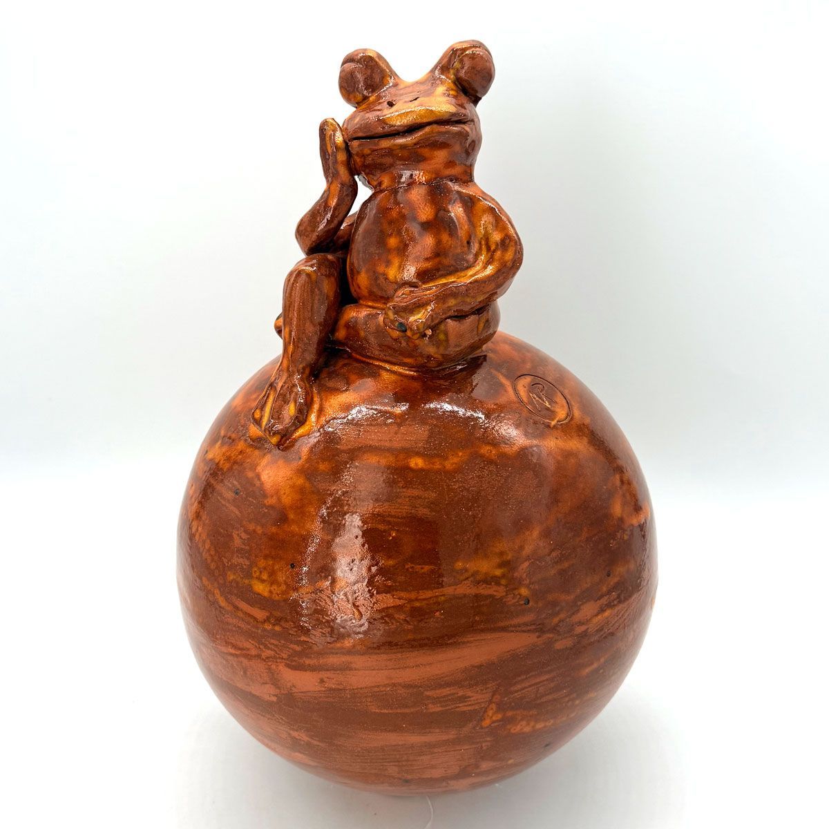 Klein bruin kikkerfiguurtje, zittend op een glanzende houten bol.