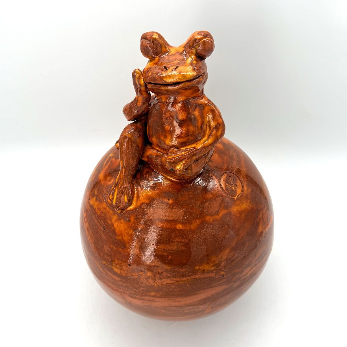 Klein bruin keramisch kikkerfiguurtje zittend op een glanzende bruine bol.