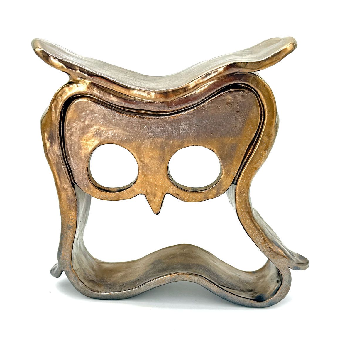 Gouden metalen masker of sculptuur in de vorm van een uil met ronde oogopeningen op een witte achtergrond.