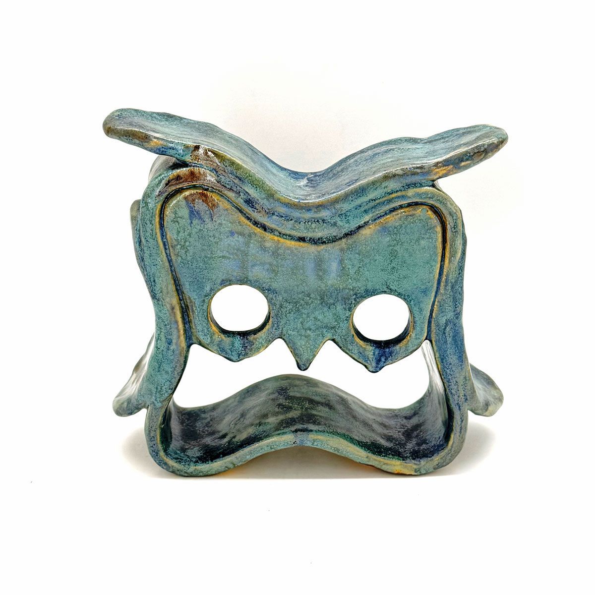 Blauwgroen keramisch masker in de vorm van een uil met twee ronde oogopeningen en een golvende, snorachtige mondopening.